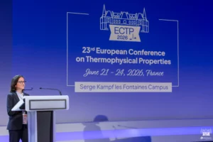 Une personne debout derrière un puptre dans un auditorium, a côté d'une présentation powerpoint intitulé "ECTP 2026"